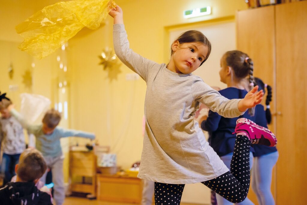 Kinder tanzen ausgelassen mit Chiffontüchern in der Hand durch einen Raum. 